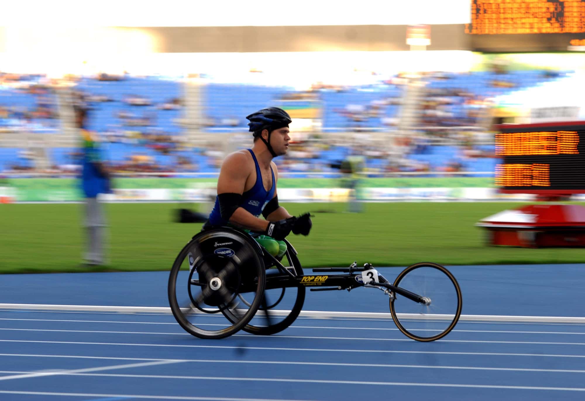 Atleta em cadeira de corrida acelera na pista azul do estádio