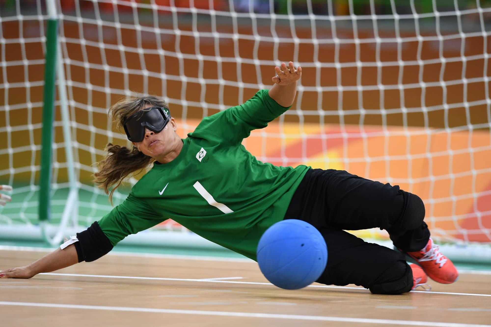 Jogadora de goalball se estica no chão da quadra para bloquear a bola