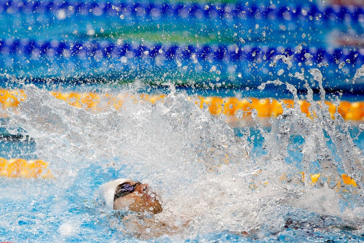 Nadador de costas avança entre borrifos de água na piscina