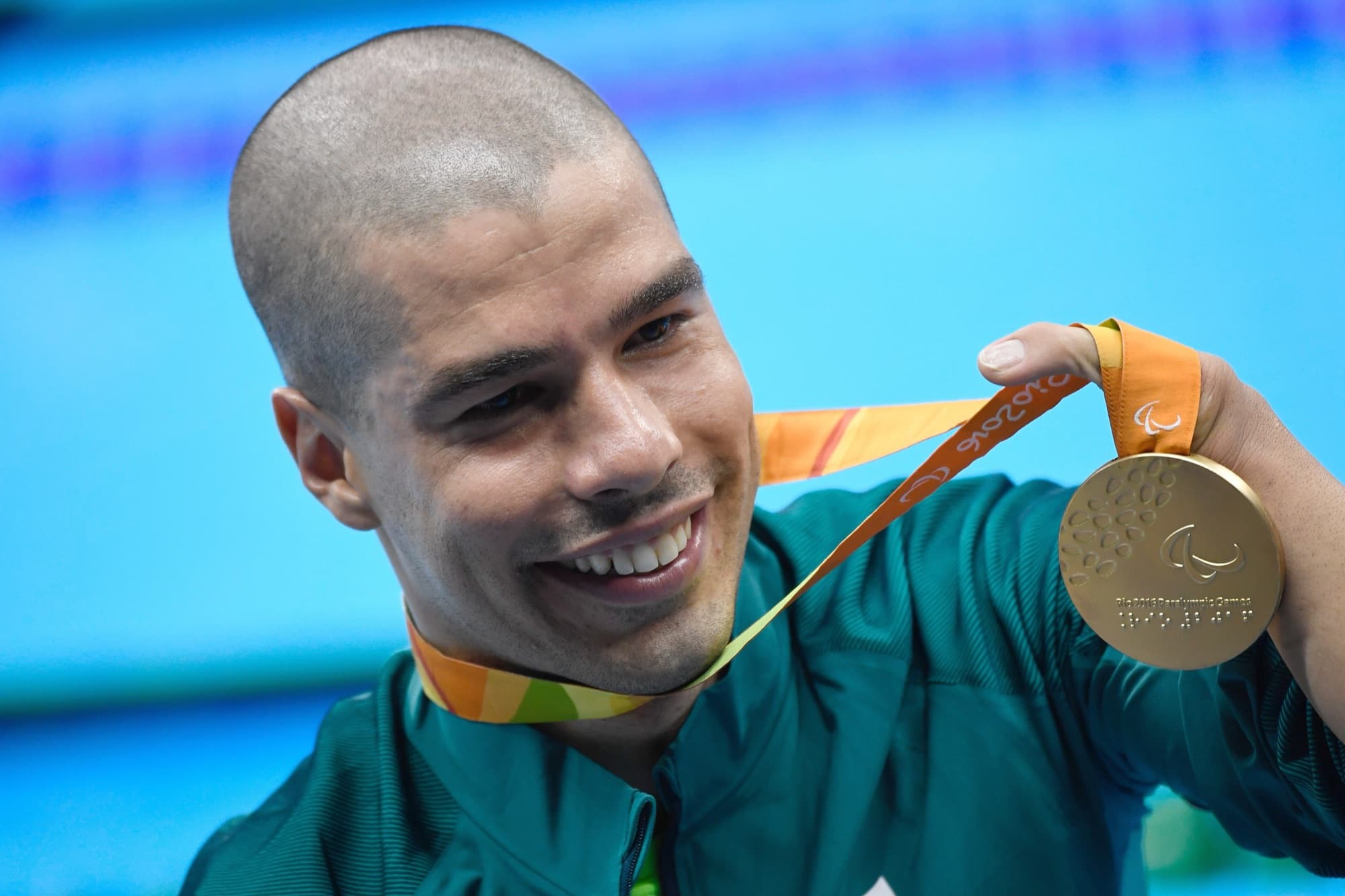 Nadador sorri e mostra a medalha de ouro à beira da piscina